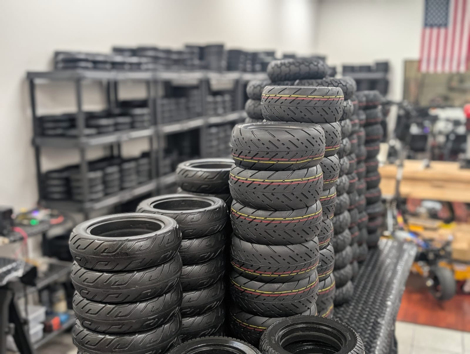 Stacks of tires in a warehouse setting with shelves and an American flag in the background.